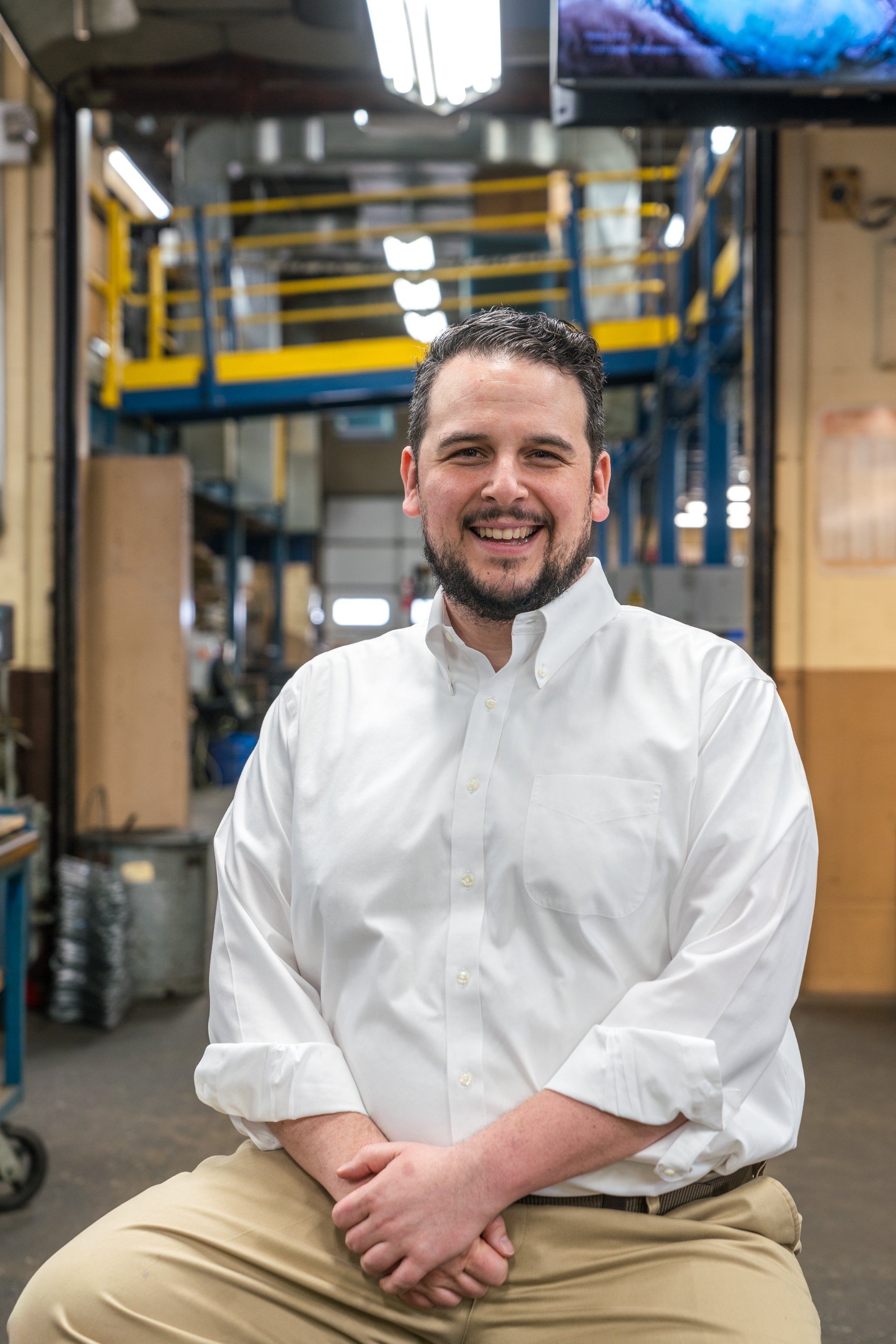 Man in a white shirt and beige pants sitting in a warehouse setting